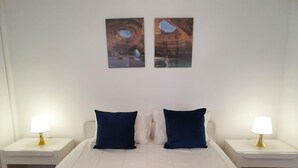 A bedroom with a white bed, two nightstands, two lamps, and two paintings on the wall.