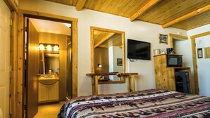 A bedroom with a wooden ceiling, a bed with a patterned bedspread, a mirror, a television, and a small kitchenette area. - Enjoy a lakeview sunset in Room 6 - The Bear's Den - Curriers Lakeview Lodge (Rice Lake)