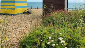 Two beach huts, one yellow and blue, and one brown, on a pebbled beach with a view of the sea.