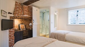 A bedroom with two beds, a brick wall, a TV, and a shower area. - A delightful cottage in the heart of the historic conservation area of Deal (Deal)