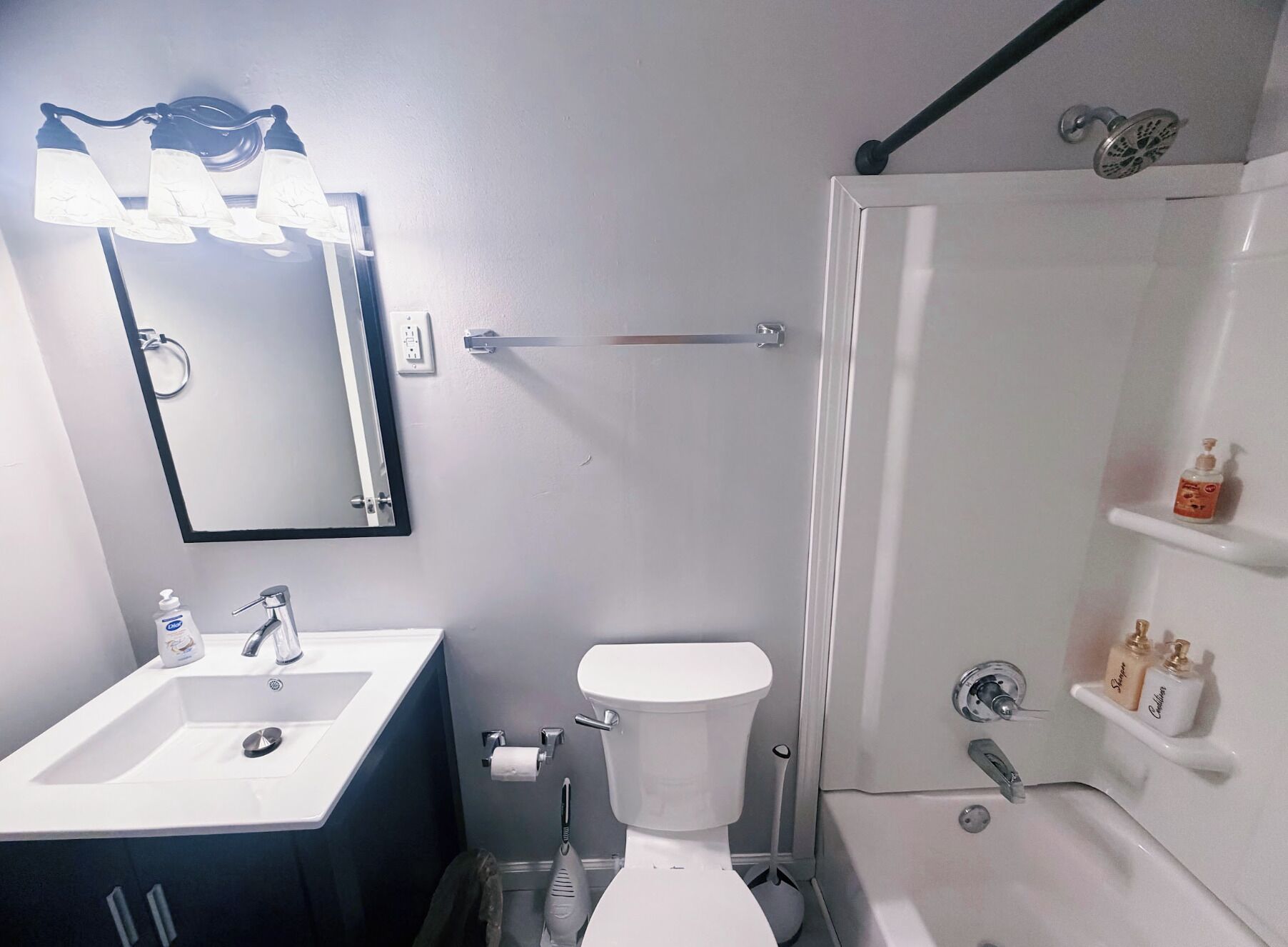 A bathroom with a white sink, toilet, and shower. There is a mirror above the sink and a towel rack on the wall.