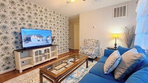 A living room with a television, a sofa, a coffee table, and a patterned wall.