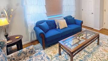 A living room with a blue sofa, a glass coffee table, a patterned rug, and a lamp.