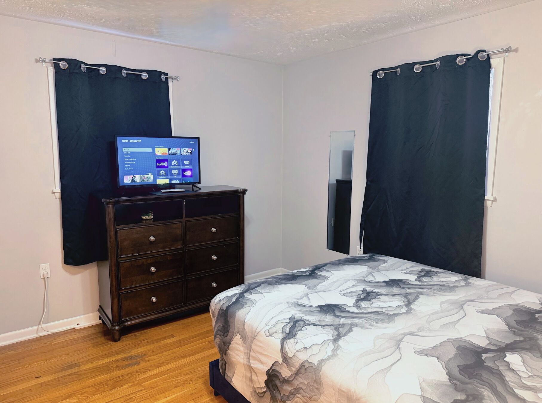 Un dormitorio con cama, cómoda, televisor y cortinas.