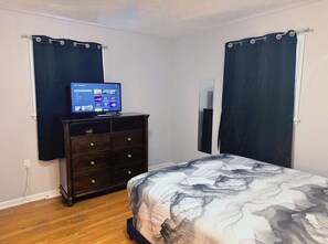 Une chambre à coucher avec un lit, une commode, une télévision et des rideaux.