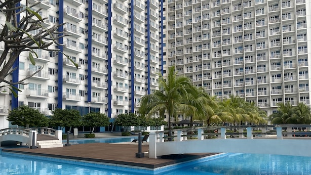 A modern hotel with a large pool area, palm trees, and a high-rise building in the background. - Jazz Tower A // Cozy Room for 2 Adults //  Best for Short stays (Makati)