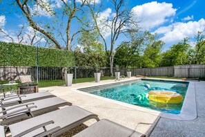 A backyard with a swimming pool, lounge chairs, and a wooden fence.