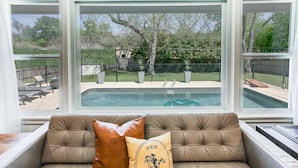 Ein Zimmer mit Blick auf einen Hinterhof-Pool, einer gepolsterten Sitzecke mit zwei Kissen und einem Fenster zum Außenbereich.