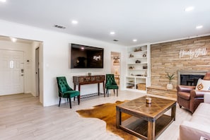 A modern living room with a wooden coffee table, green chairs, a fireplace, and a mounted TV.