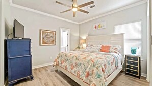 Une chambre à coucher avec un lit, un ventilateur de plafond, une commode et une fenêtre avec des stores.