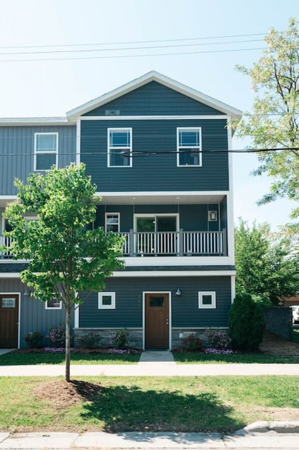 A two-story residential building with a front porch, a small tree, and a well-maintained lawn. - Lakescape Modern 3BD Townhome Downtown Wineries (Traverse City)
