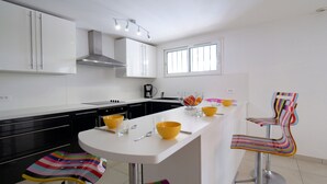 A modern kitchen with white cabinets, a black countertop, and a central island with stools. - French Riviera Air-conditioned Villa with heated infinity pool, Amazing view (Var)