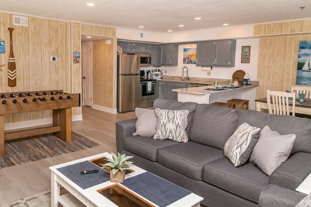 A modern living room with a grey sofa, wooden accents, and a foosball table.