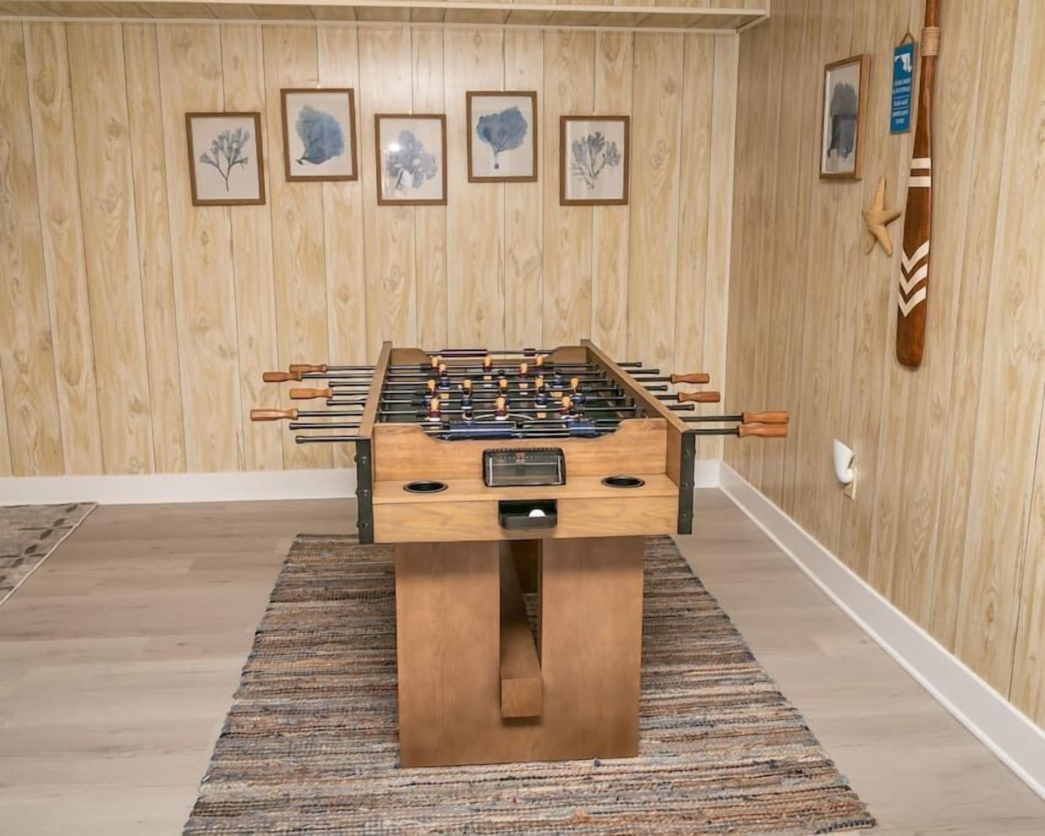 A foosball table in a room with wooden walls and framed artwork.