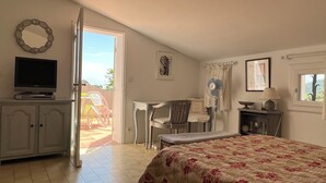 Quarto com cama, televisão, escrivaninha, cadeira, ventoinha e janela.