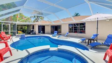 A swimming pool with lounge chairs and umbrellas, surrounded by a covered area with a view of palm trees.