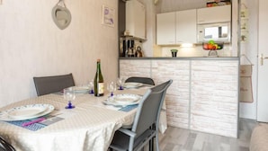 Un coin repas avec une table dressée pour quatre personnes, une bouteille de vin et une cuisine visible au fond.