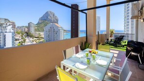 Un balcon avec une table dressée pour le dîner, offrant une vue sur un paysage urbain côtier dominé par une montagne imposante.