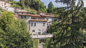 Uma villa numa encosta com fachada de pedra, várias varandas e um jardim exuberante.