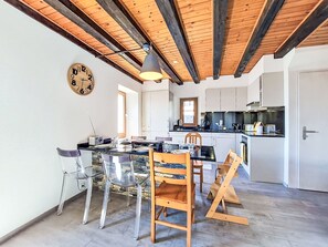 A modern kitchen with white cabinets, a wooden ceiling, and a dining area with clear chairs and a wooden table. - Tilleul by Interhome (Grimisuat)