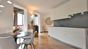 Une cuisine moderne avec des armoires blanches, une hotte en acier inoxydable et un coin repas comprenant une table ronde et des chaises.