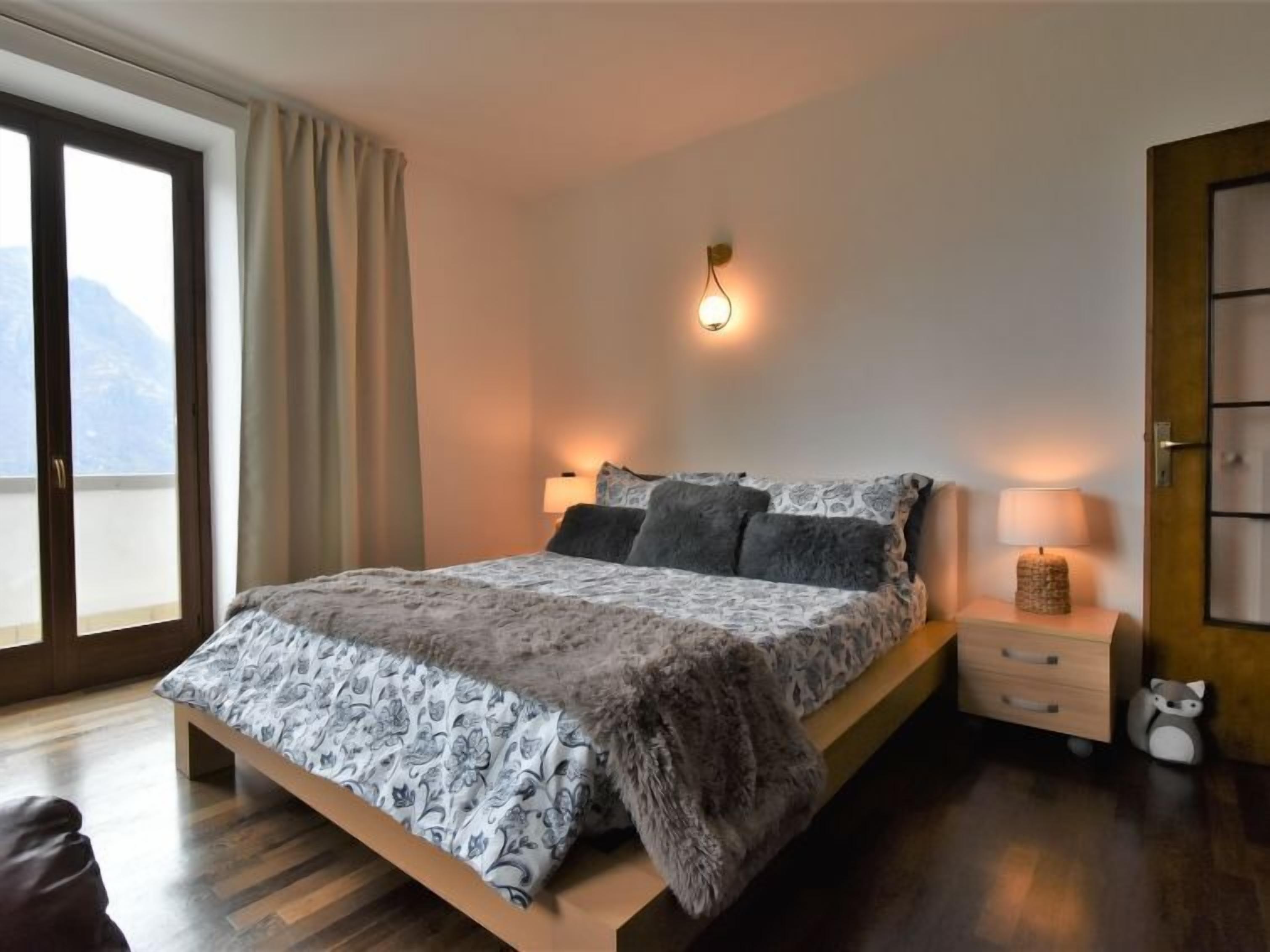 Un dormitorio moderno con una cama grande, dos mesitas de noche, una lámpara de pared y vistas a través de un ventanal corredera.