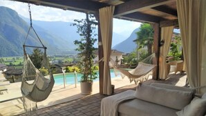 Un espace extérieur accueillant, aménagé avec un canapé et des hamacs suspendus, offrant une vue sur une piscine et des montagnes.