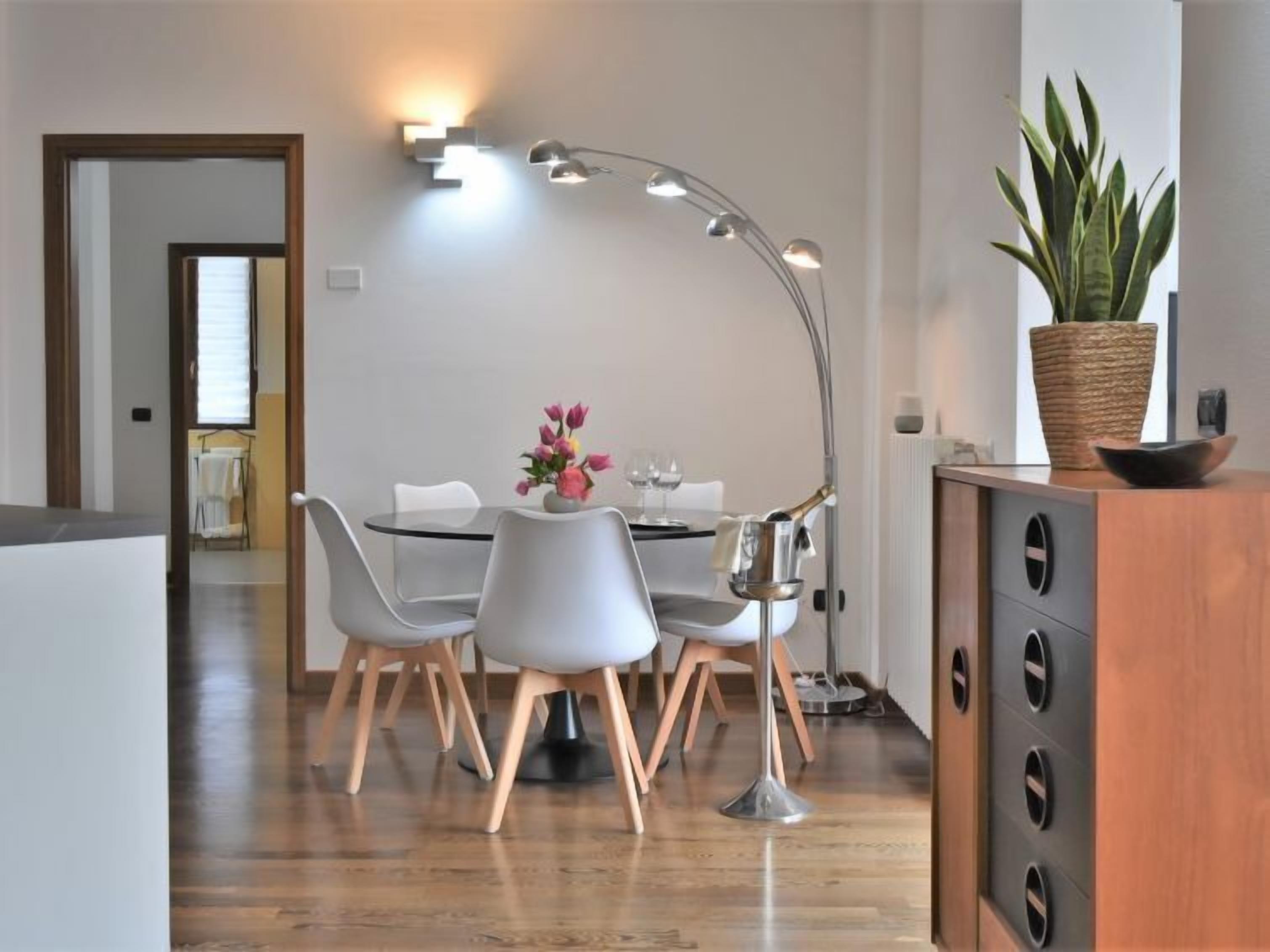 A modern dining area with a round table, four chairs, a tall floor lamp, and a potted plant.