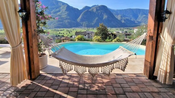Un hamac sous une pergola en bois, avec vue sur un paysage montagneux et une piscine.