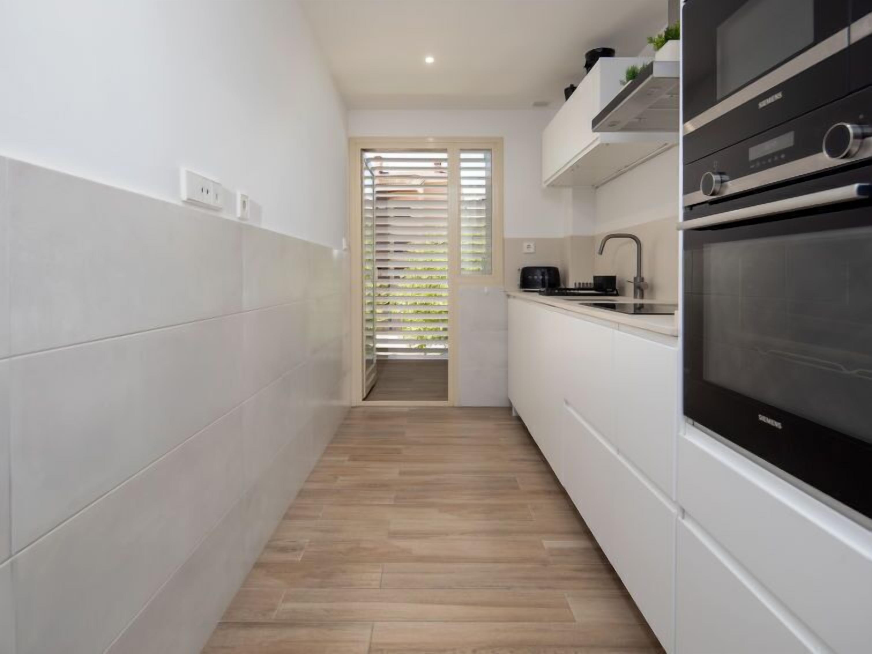 A narrow kitchen with white cabinets, a black oven, and a wooden floor.
