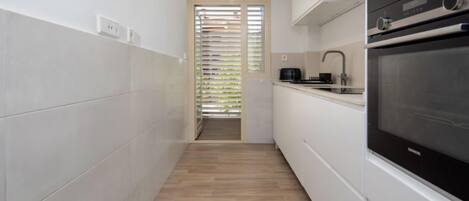 A narrow kitchen with white cabinets, a black oven, and a wooden floor.