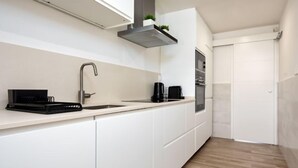 Una cocina moderna con armarios blancos, un lavamanos de acero inoxidable, una cafetera negra y un horno empotrado.