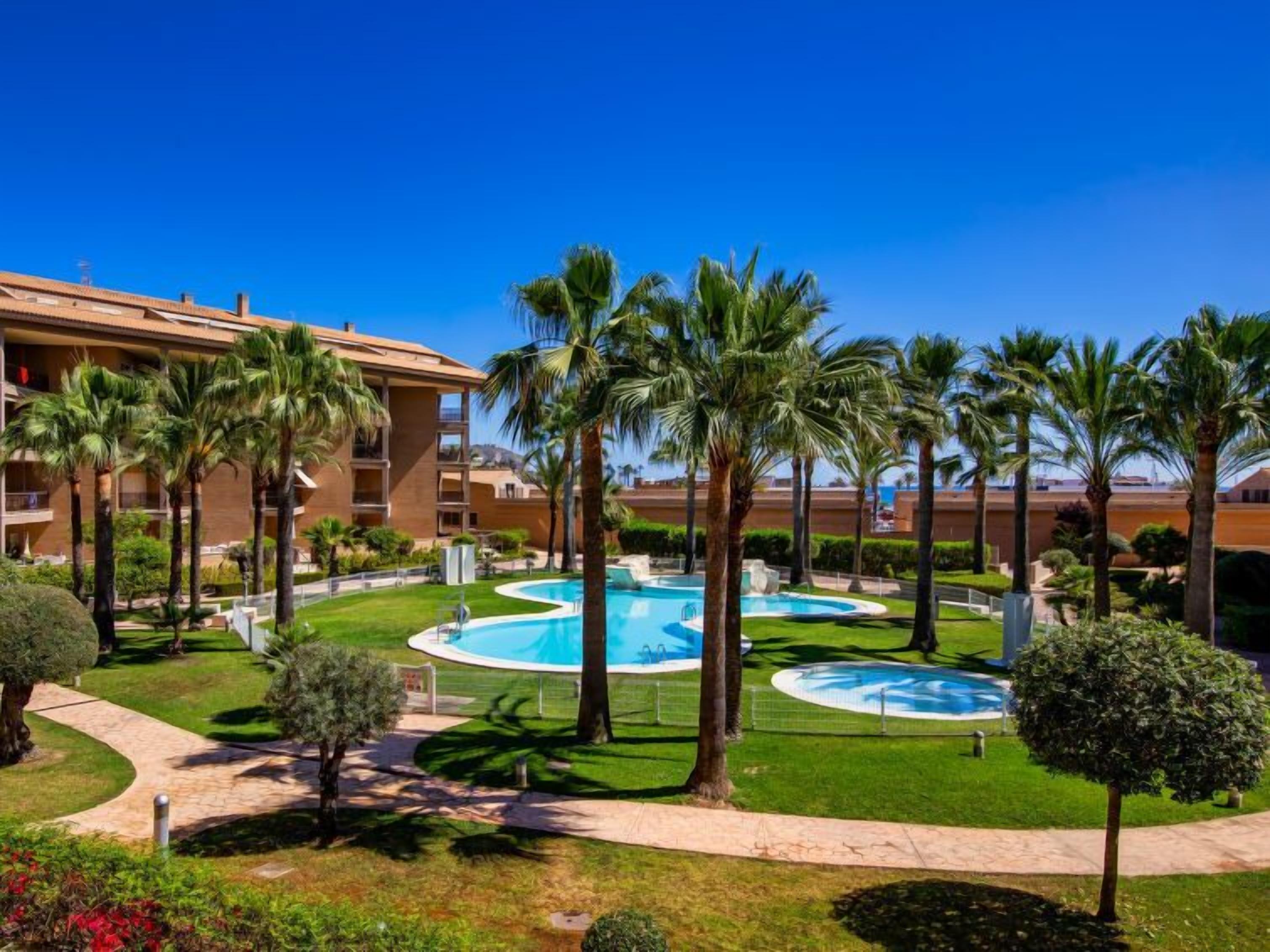 Un hôtel doté de plusieurs piscines, entouré de palmiers et d’une pelouse bien entretenue.