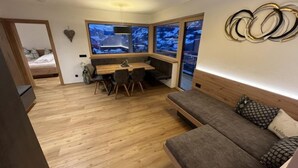 Ett kompakt rum med trägolv, en soffa, ett matbord med stolar och ett stort fönster med utsikt.