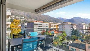 A balcony with a table and chairs, overlooking a cityscape with mountains in the background. - LocTowers A3.4.3 by Interhome (Locarno)