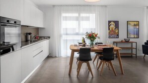 Een moderne keuken met witte kasten, een ingebouwde oven en een eethoek met een houten tafel en stoelen.