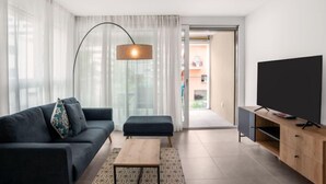 Un salon moderne comprenant un canapé, un pouf, une table basse, un téléviseur et une lampe.