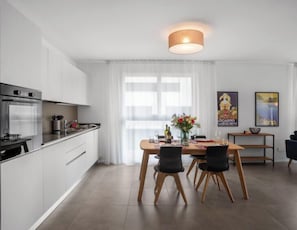 A modern kitchen with white cabinets, a built-in oven, and a dining area with a wooden table and chairs.
