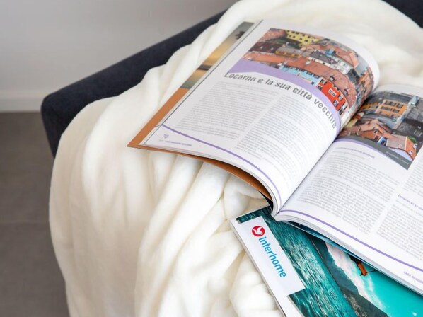 A book open on a white, textured surface, possibly a bed or couch, with a visible logo on the cover.