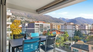 A balcony with a table and chairs, overlooking a cityscape with mountains in the background. - LocTowers A3.4.2 by Interhome (Locarno)