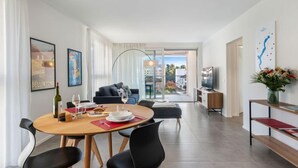 A modern living room with a round wooden table, black chairs, a sofa, and a TV. There is a balcony with a view of buildings. - LocTowers A4.2.3 by Interhome (Locarno)