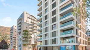 Un edificio residenziale moderno a più piani, con balconi, un cortile curato e uno sfondo montuoso.