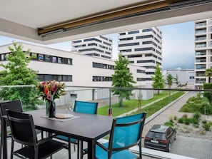 A balcony with a table and chairs, overlooking a residential area with modern buildings and greenery.