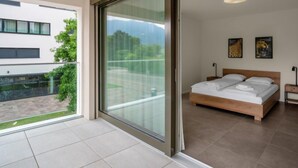 Een moderne slaapkamer met een grote schuifpui naar een balkon, een bed met witte lakens, en twee ingelijste foto’s aan de muur.