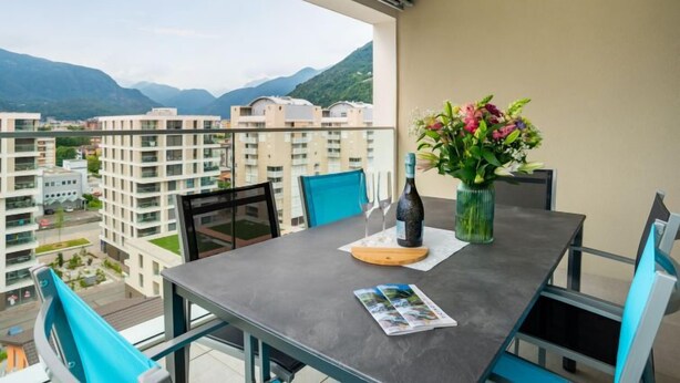 A balcony with a table, chairs, a vase with flowers, and a bottle. - LocTowers A4.8.2 by Interhome (Locarno)