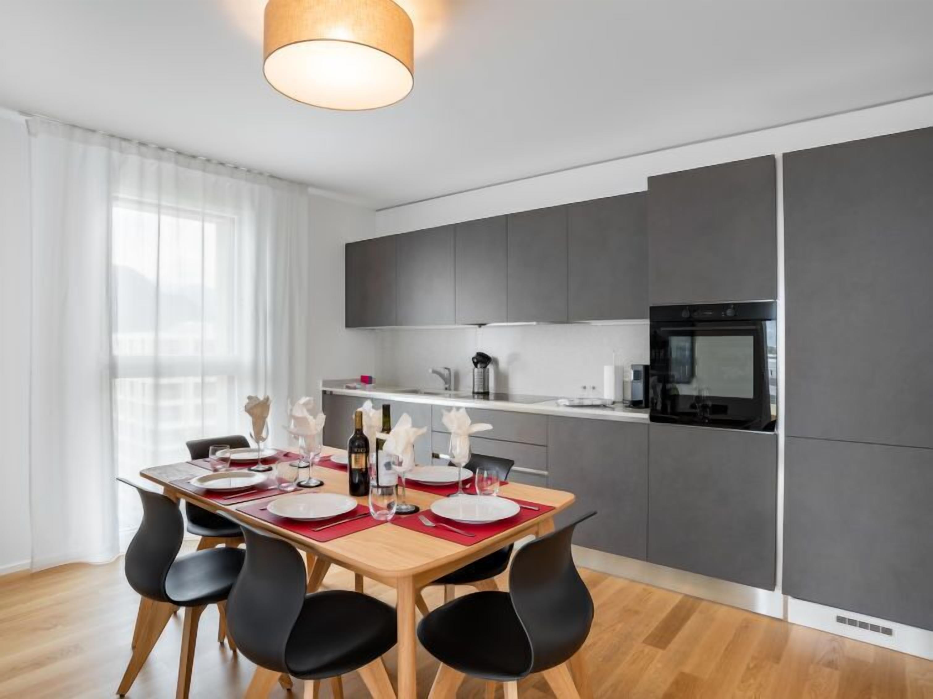 A modern kitchen with grey cabinets, a built-in oven, and a dining area with a wooden table set for four.