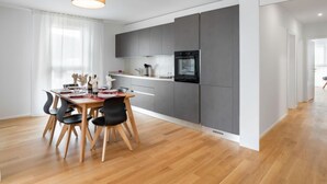 Una cucina moderna con mobili grigi, forno integrato e zona pranzo con tavolo e sedie in legno.