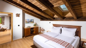 A bedroom with a wooden ceiling, a skylight, a bed with white bedding, a wooden dresser, and a small table with a lamp.