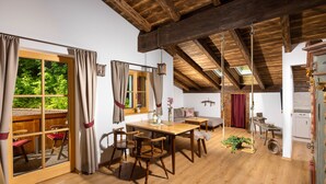 A rustic room with wooden beams, a dining table with chairs, a sofa, and a small kitchen area.