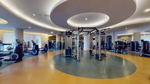 Ein modernes Fitnessstudio mit unterschiedlichen Trainingsgeräten, einem zentralen, kreisförmigen Design im Boden und einer großzügigen Gestaltung.
